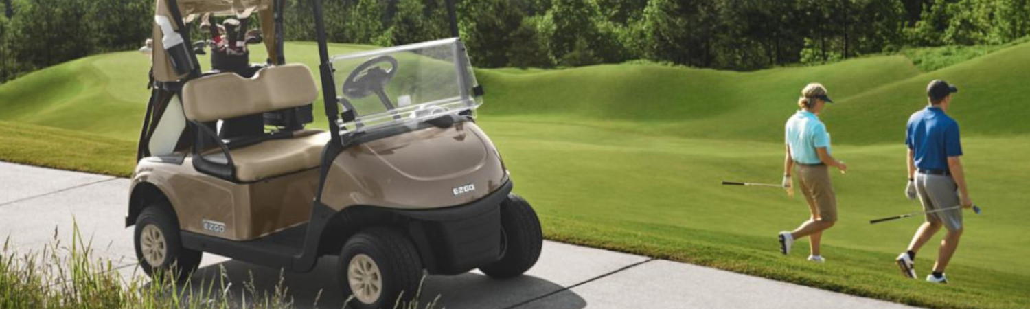 Two people carrying golf clubs walking down a hill away from a 2019 E-Z-GO RXV golf cart parked …